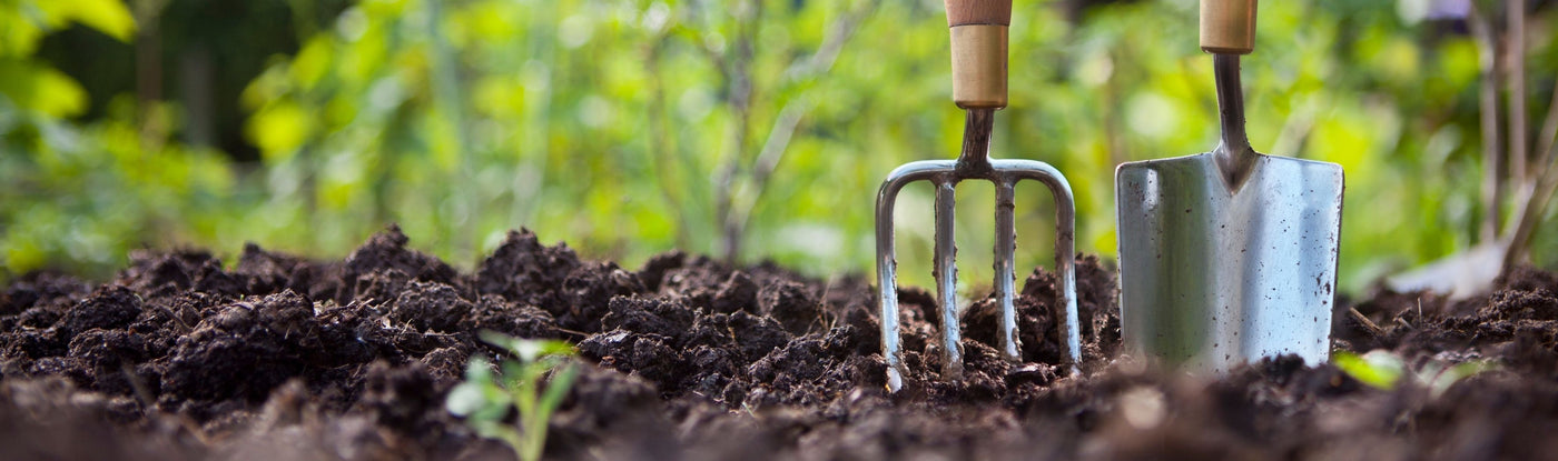 Gartenwerkzeuge wie Handschaufel und Grabgabel von NOOR stecken einsatzbereit in lockerer Erde.