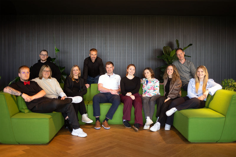 Eine Gruppe von Erwachsenen Menschen sitzt auf einer Grünen Couch und schaut in die Kamera