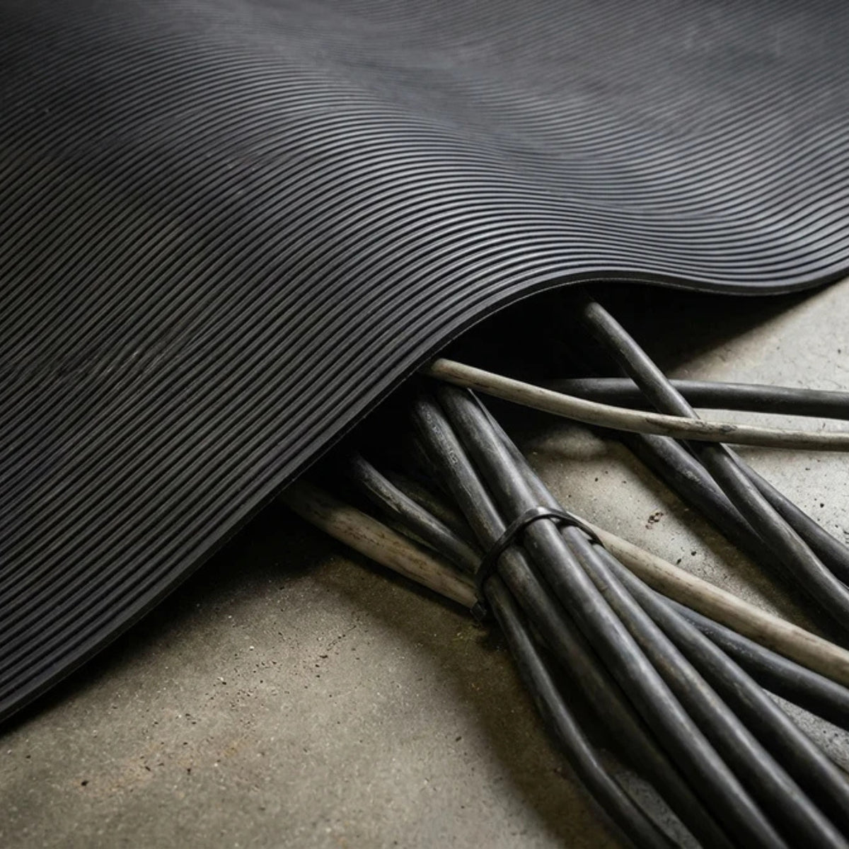 Flexible schwarze Riefenmatte liegt über mehreren Kabeln und schützt sie auf einem Betonboden.