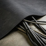 Flexible schwarze Riefenmatte liegt über mehreren Kabeln und schützt sie auf einem Betonboden.