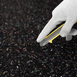 Eine behandschuhte Hand schneidet die schwarze Gummigranulatmatte mit einem Cuttermesser passgenau zu.
